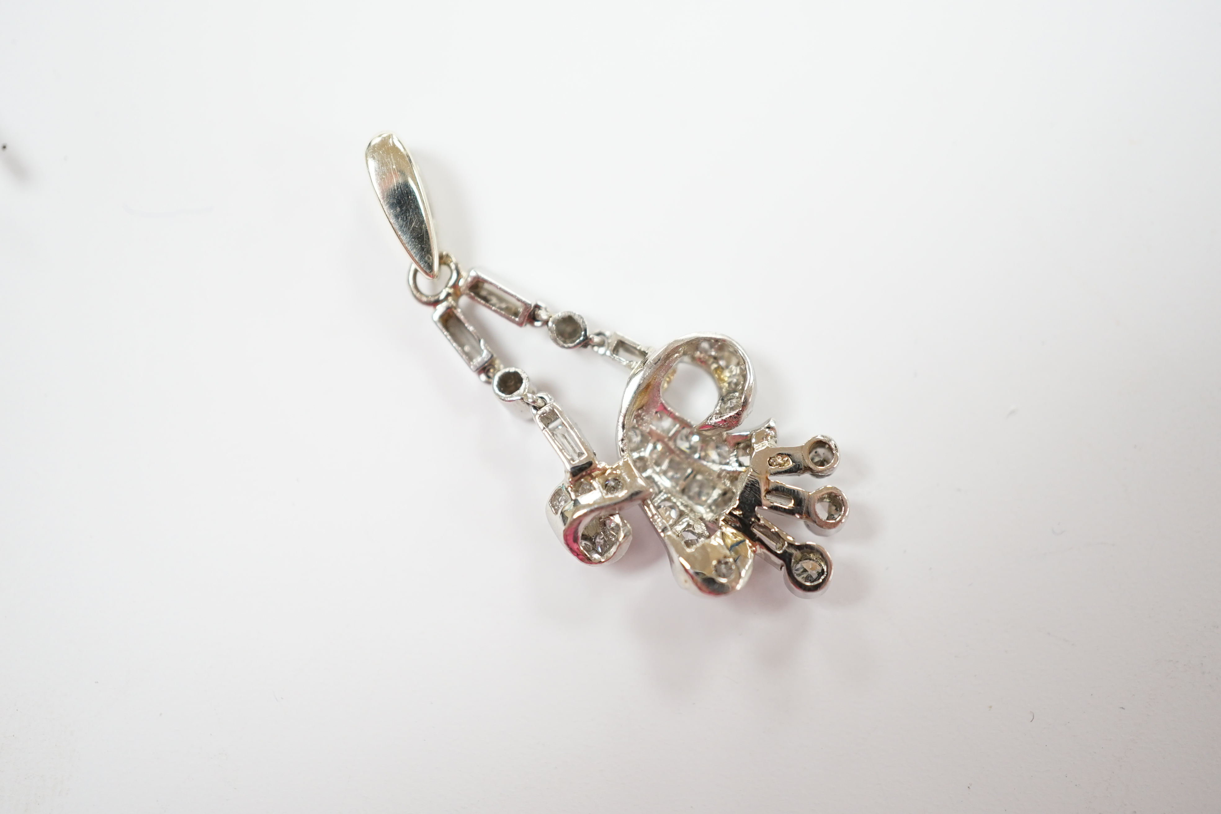 A white metal baguette and round cut diamond cluster set scroll pendant, overall 33mm, gross weight 3.6 grams.